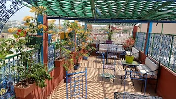 Una terraza en la azotea con una pérgola verde, plantas en macetas y mobiliario exterior.