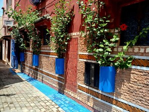A building with a red facade, blue window shutters, and a tiled ground.