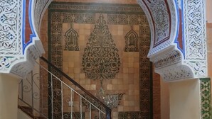 A staircase with ornate white and blue patterns, a tiled wall with a central design, and a large vase at the bottom. - Riad Idrissi (Meknes)