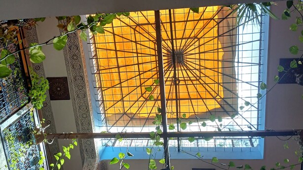 A room with a high ceiling, ornate metal railings, and a large window with a geometric patterned glass design. - Riad Idrissi (Meknes)