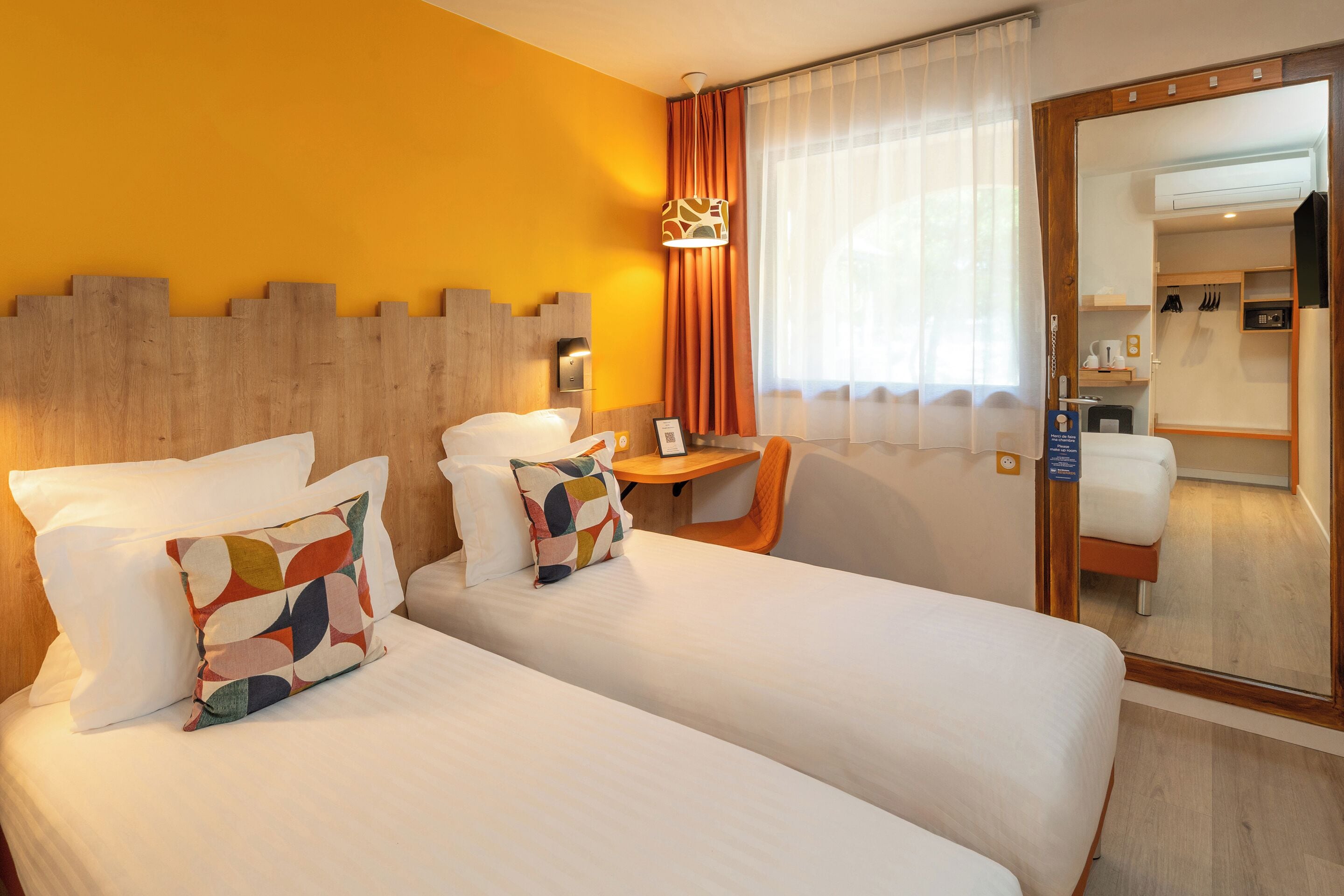Une chambre d’hôtel avec deux lits, une petite table, une chaise, un miroir et une vue sur la salle de bain.