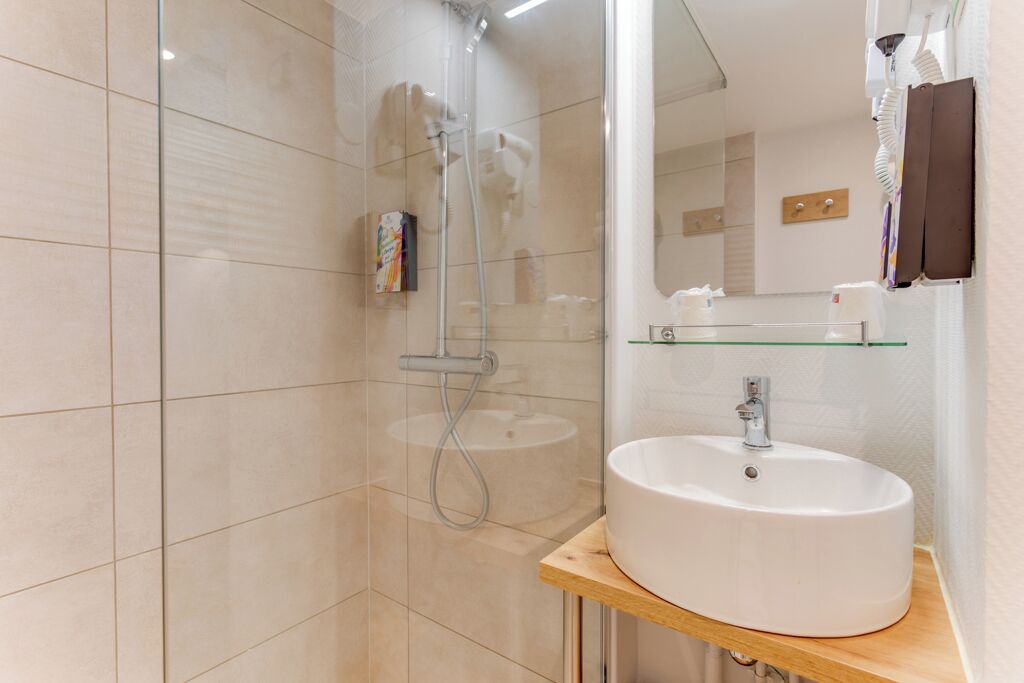 Un baño moderno con cabina de ducha de vidrio, un lavamanos blanco sobre encimera de madera y un espejo sobre el lavamanos.