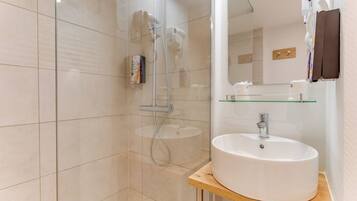 Un baño moderno con cabina de ducha de vidrio, un lavamanos blanco sobre encimera de madera y un espejo sobre el lavamanos.
