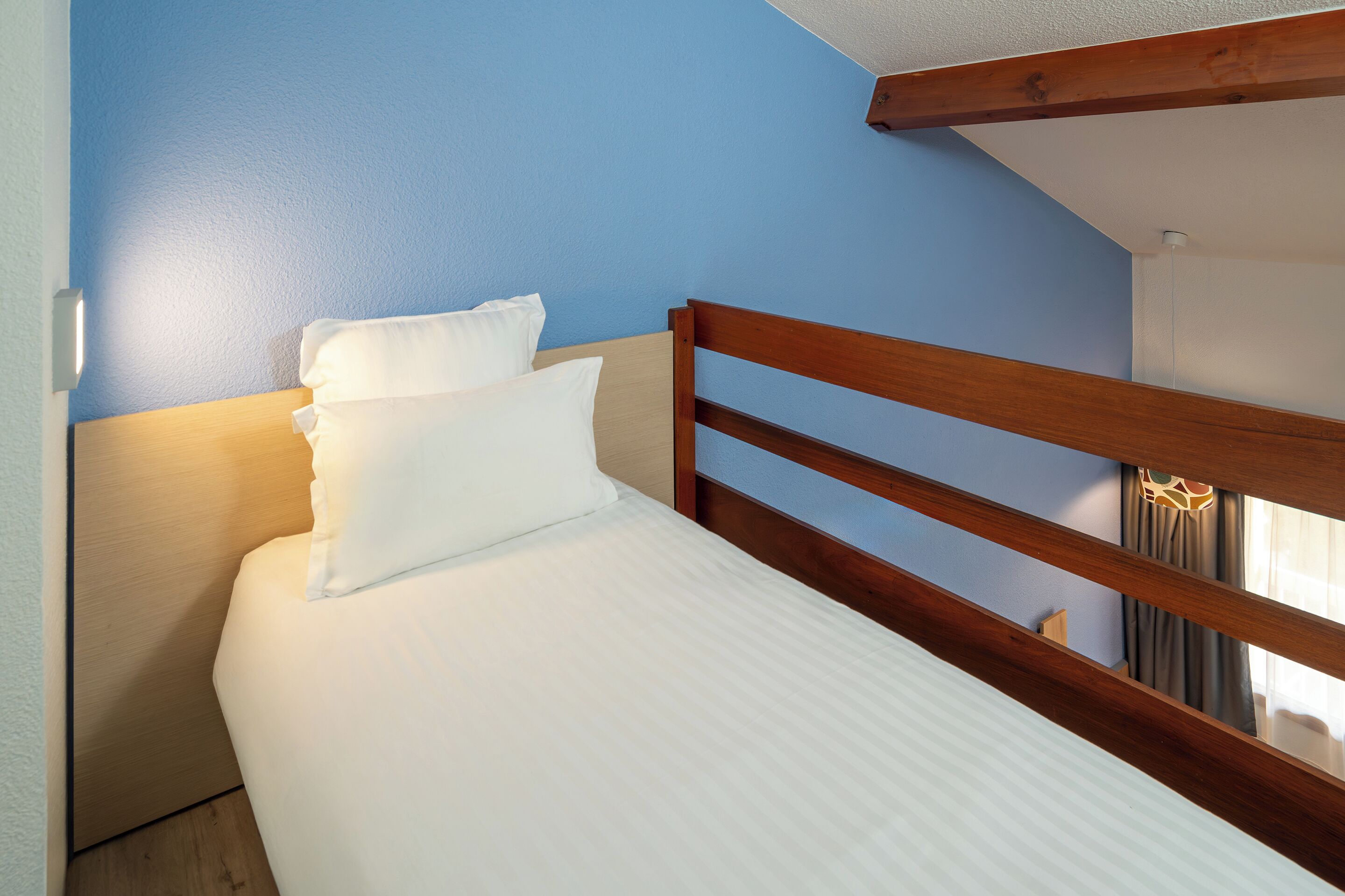 A neatly made bed with white linens in a room with blue walls and wooden headboard.