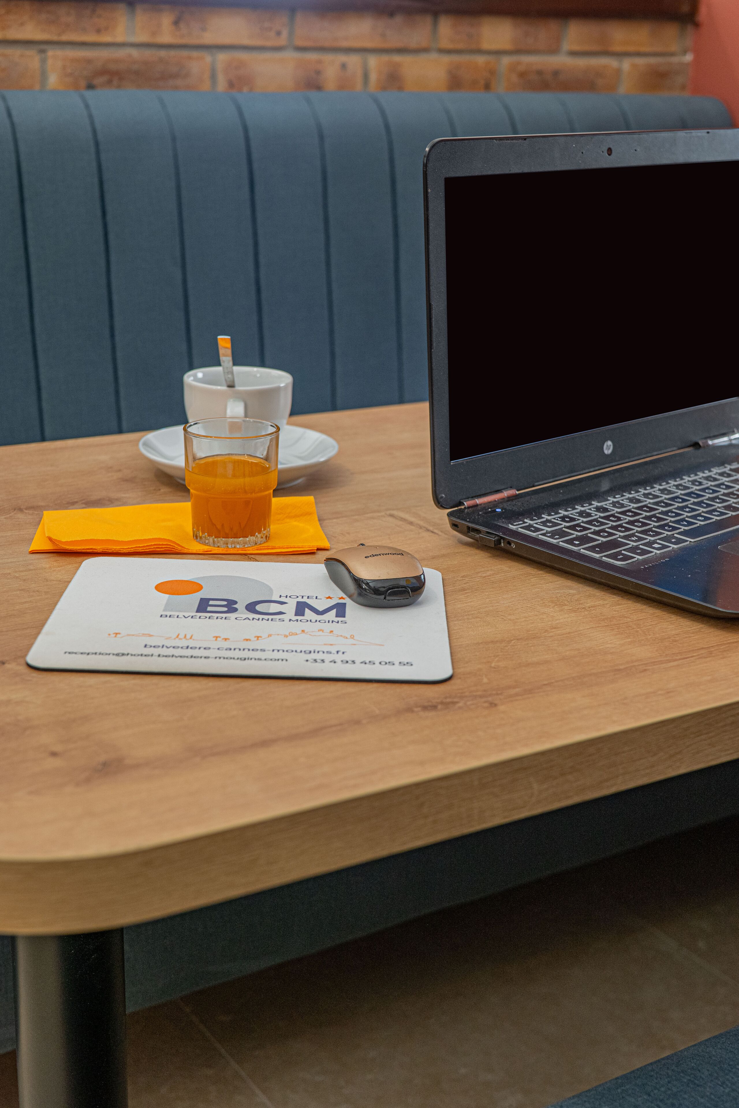 Ein Laptop auf einem Holztisch zusammen mit einem Glas Orangensaft, einem Servietten und einer Hotelbroschüre.