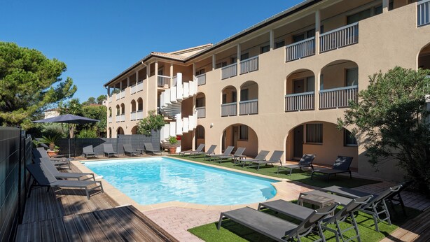 A pool area with lounge chairs, a wooden deck, and a building with balconies.