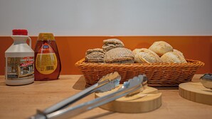 Una cesta de pan, una botella de sirope y una botella de kétchup sobre una mesa de madera.