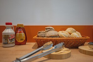Een mand met brood, een fles siroop en een fles ketchup op een houten tafel.