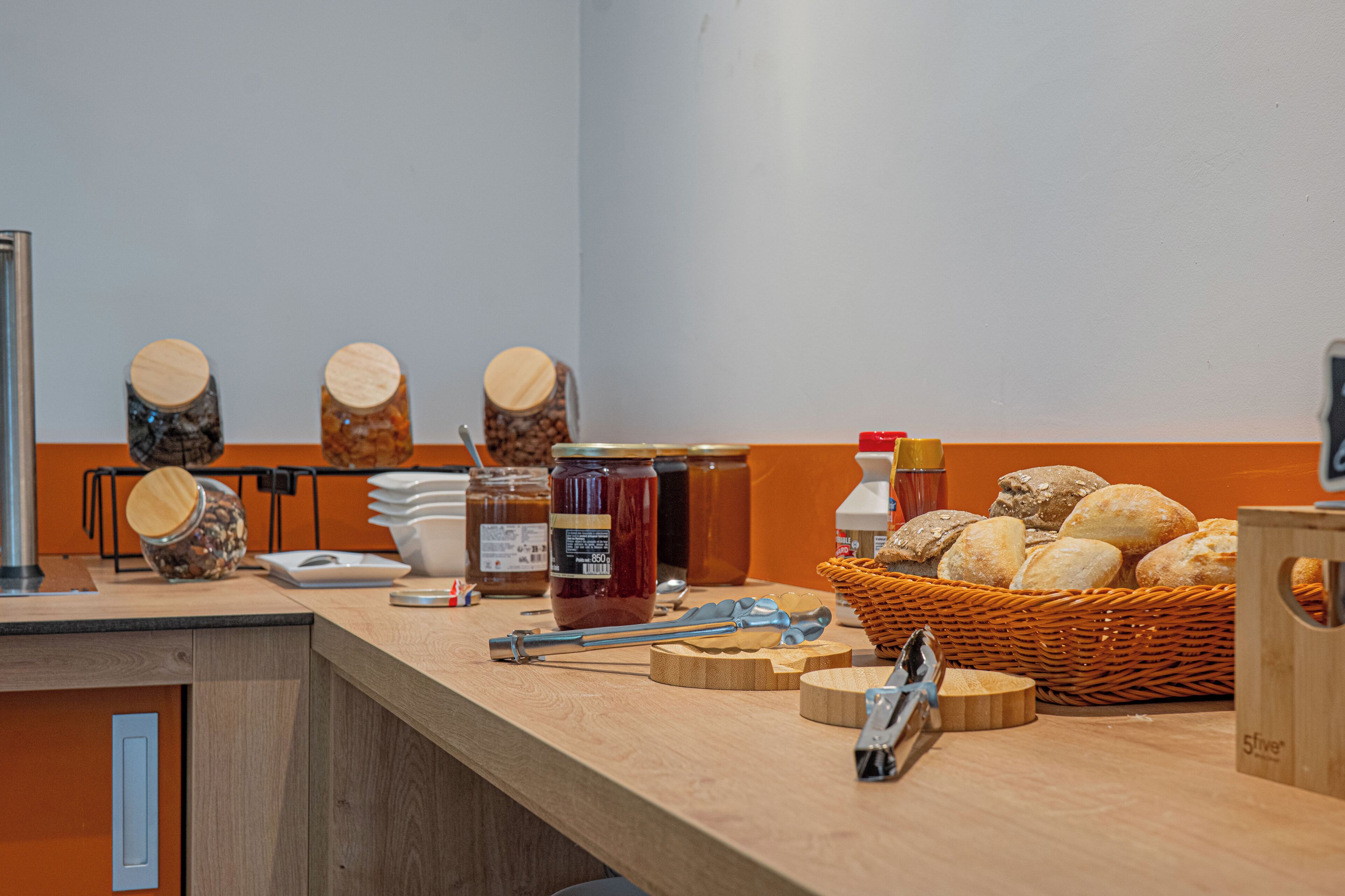 Een ontbijtbuffet met potten jam, een broodmand en een koffiehoek.