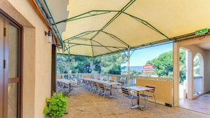 Un área de estar al aire libre techada con mesas y sillas, vista a árboles y un letrero que dice "HOTEL Belvedere".