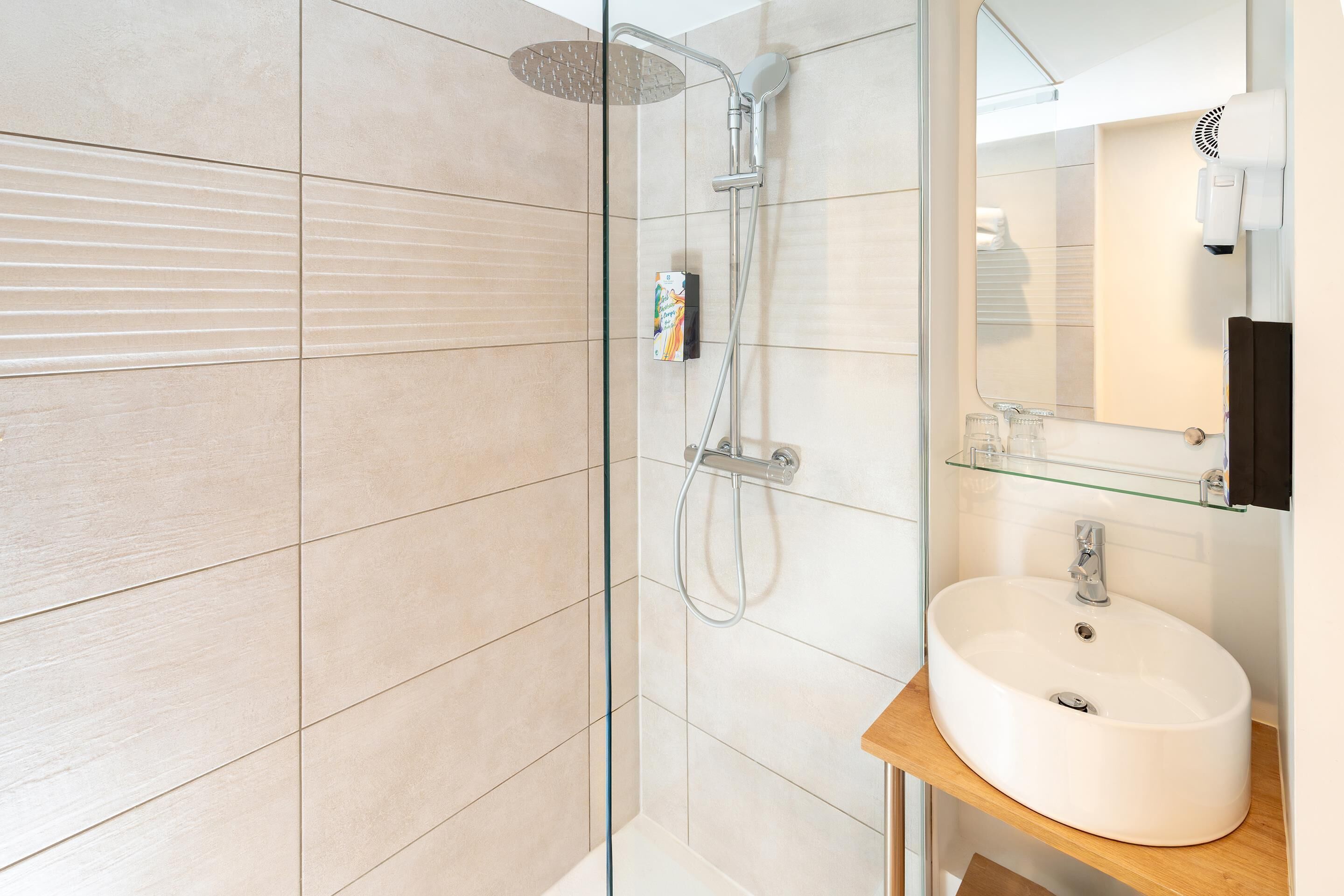 A modern bathroom with a glass shower enclosure, a white sink, and a mirror above it.