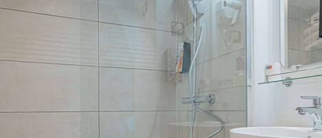 A modern bathroom with a glass shower enclosure, a white sink, and a wooden shelf.