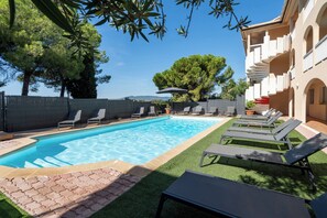 Une piscine entourée d’une clôture et d’arbres, avec des chaises longues et une pelouse artificielle.