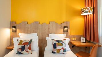 Une chambre d’hôtel avec deux lits, une tête de lit en bois, un petit bureau et une lampe fixée au mur.