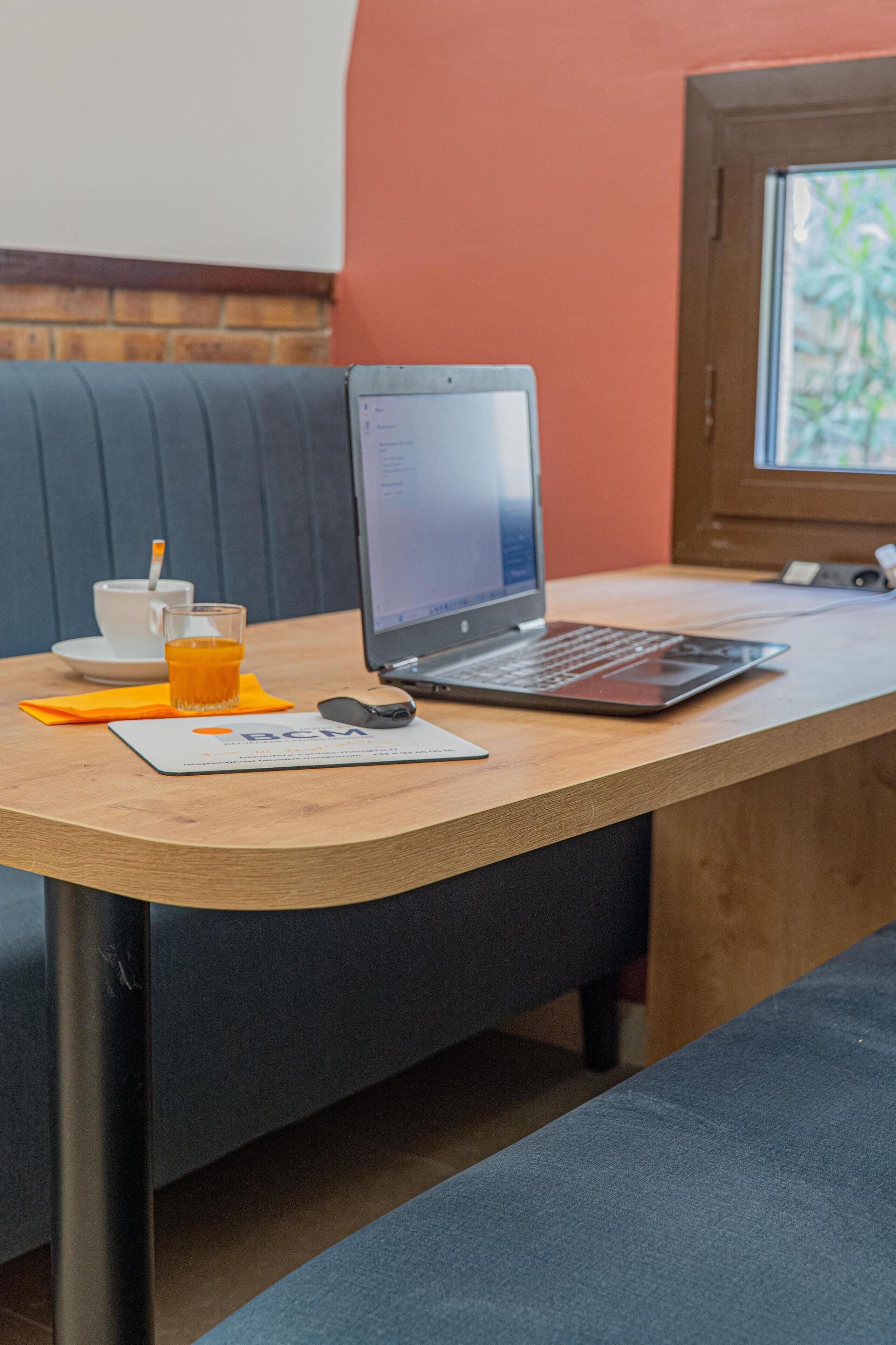 Een laptop op een houten tafel met een kop koffie en een glas sinaasappelsap.