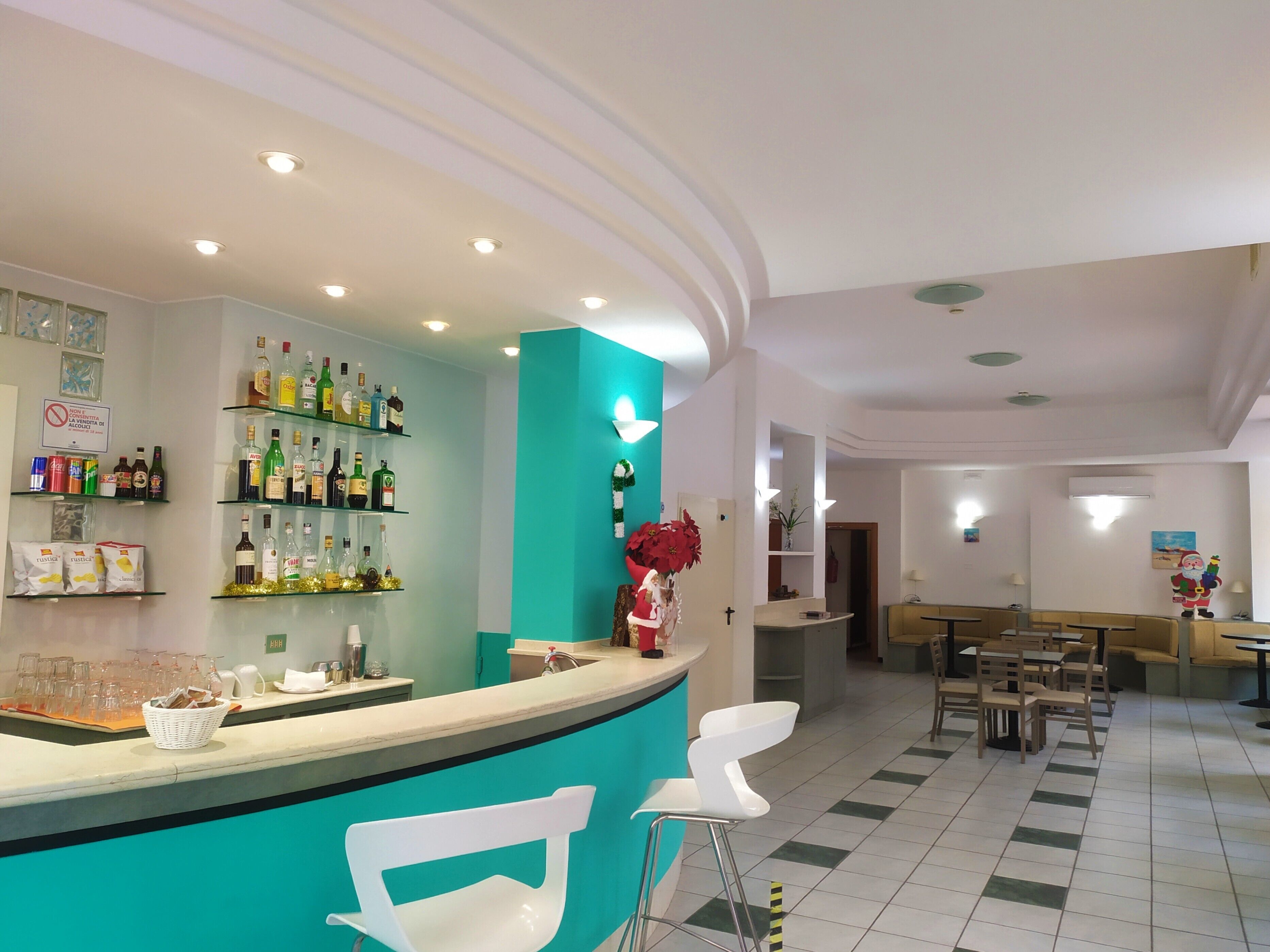 Un área de bar con estantes llenos de botellas de licor, una barra con una silla blanca y una pared de acento color turquesa.