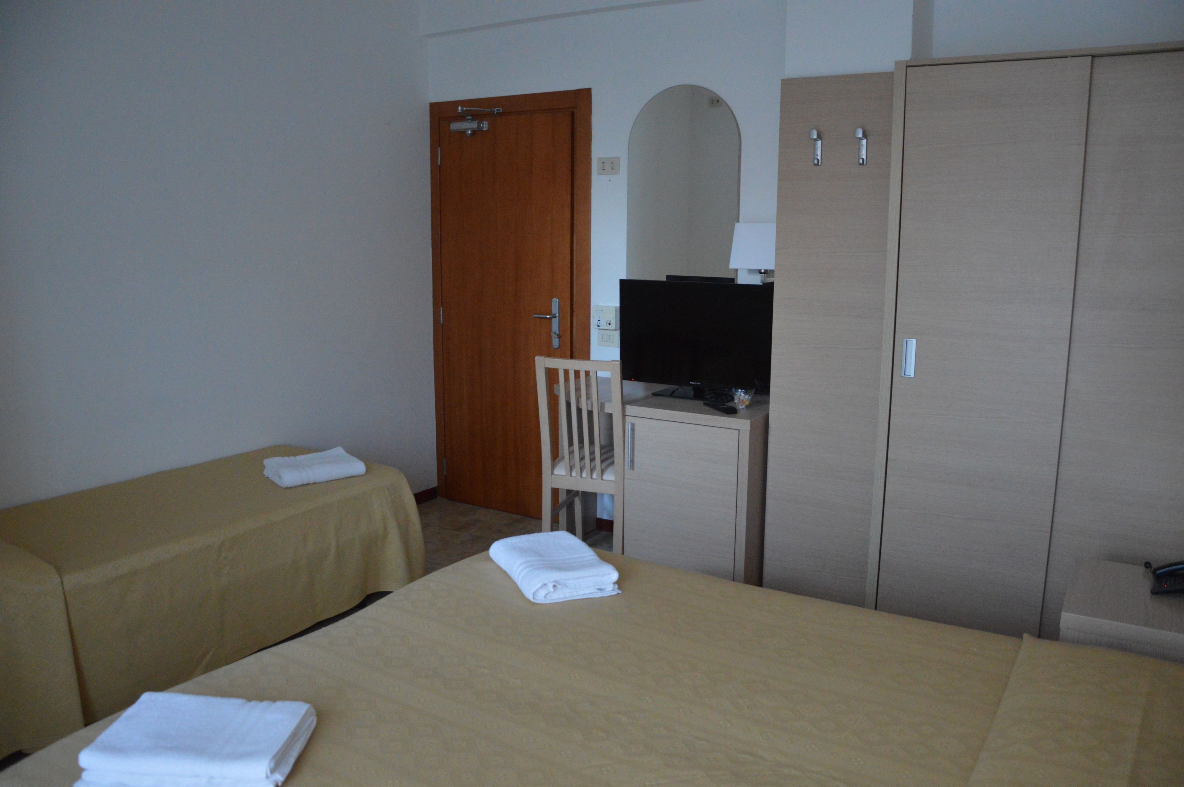 A hotel room with two beds, a desk with a computer, a wardrobe, and a door.