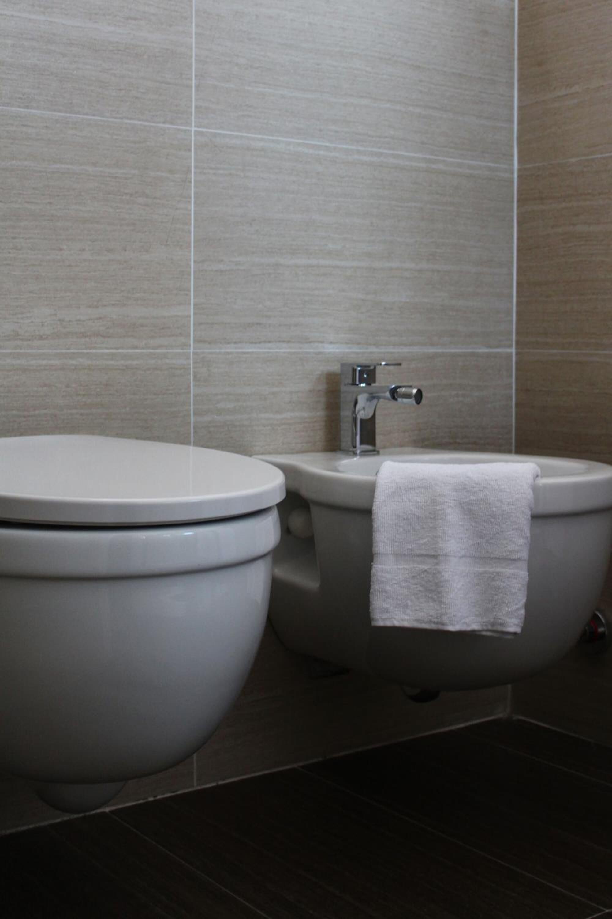 Ein modernes Badezimmer mit Toilette und Bidet, beide mit weißen Deckeln, sowie ein Handtuch an dem Bidet.
