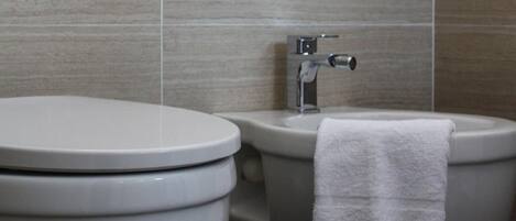 Un baño moderno con inodoro y bidé, ambos con tapas blancas, y una toalla colgada en el bidé.