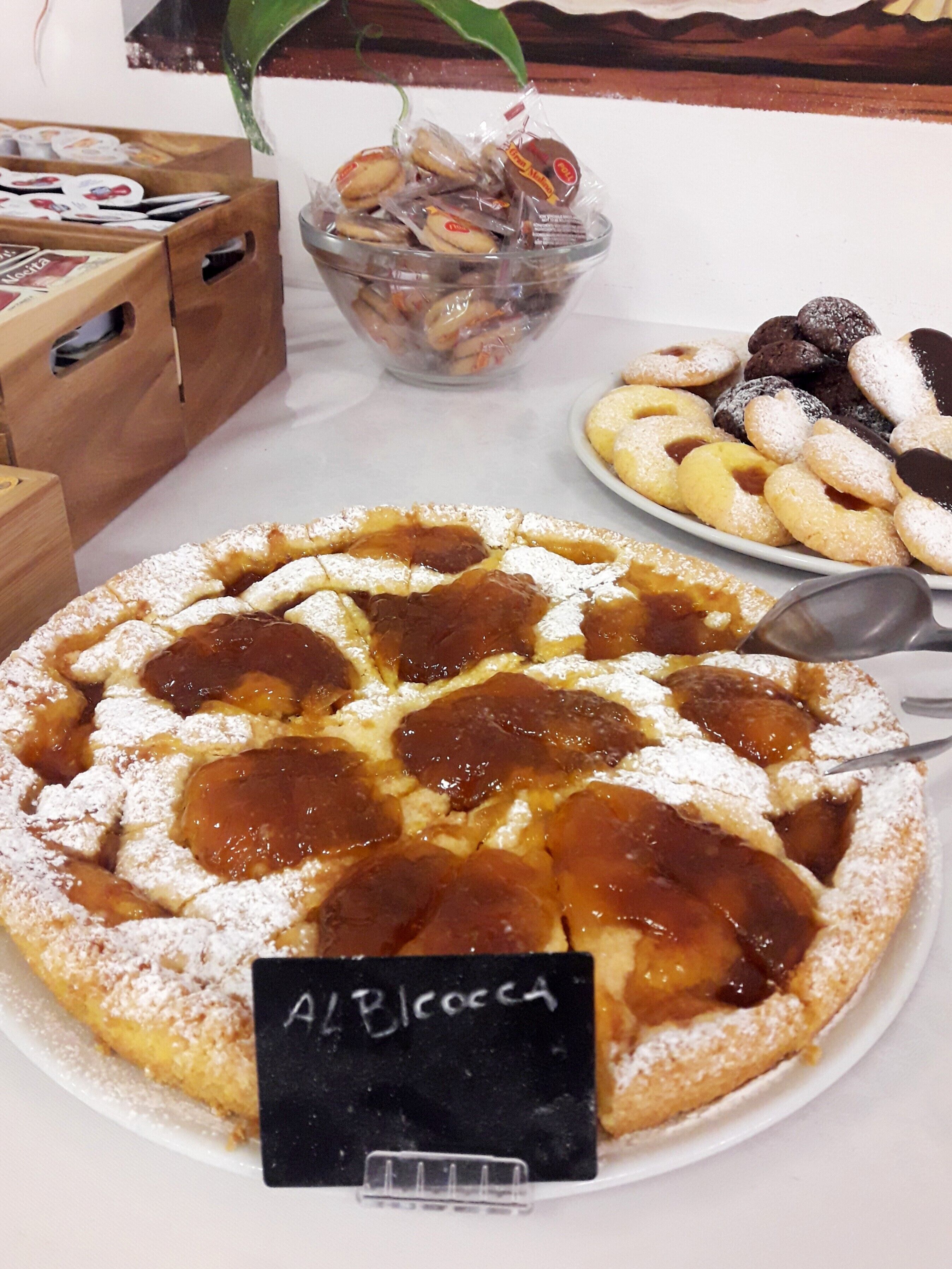 A dessert display with a variety of pastries, including a large apple cake labeled "A/Bloccca".