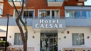 Hotelli nimeltä Hotel Caesar, jossa on moderni julkisivu, suuret ikkunat ja lasikaiteilla varustettu parveke.