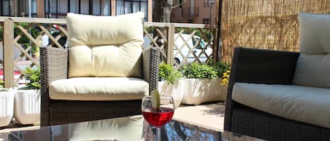 A wicker sofa with a cushion, a glass table with a red drink, and a view of a building in the background.