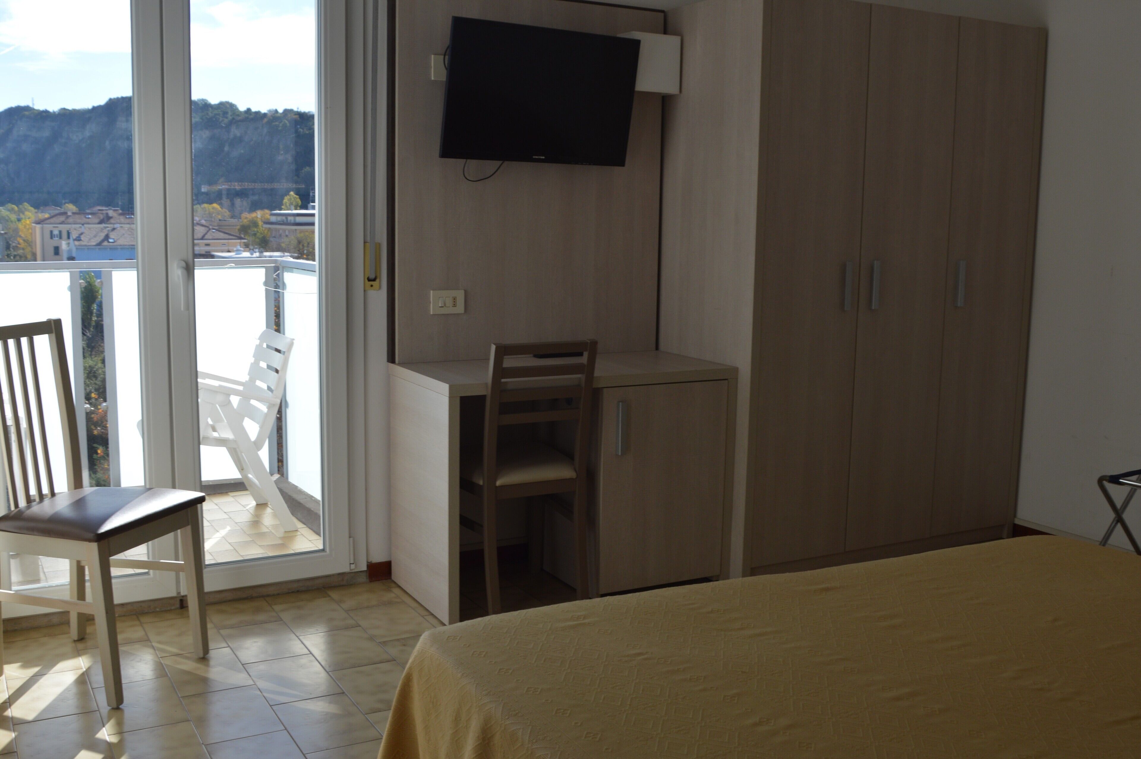 A bedroom with a bed, a desk, a chair, a wardrobe, and a TV.
