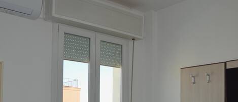 A bedroom with a bed, a ceiling fan, a wardrobe, and a view of the outside.