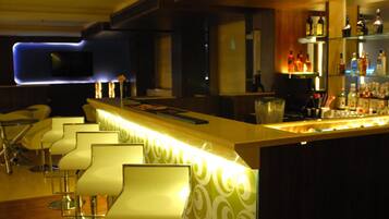 A bar area with a long counter, bar stools, and shelves with bottles.