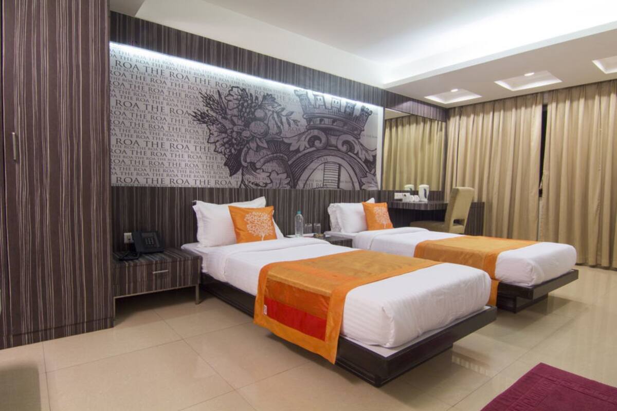 Habitación de hotel con dos camas, un tapiz grande en la pared, un escritorio con una silla y una ventana con cortinas.