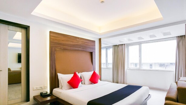 A hotel room with a large bed, a wooden headboard, a bedside table, a TV, and a window with curtains. - The Roa (Mumbai)