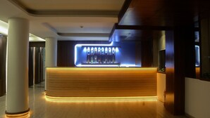 A modern reception area with a wooden reception desk, illuminated by under-counter lighting, and a row of bottles behind it. - The Roa (Mumbai)