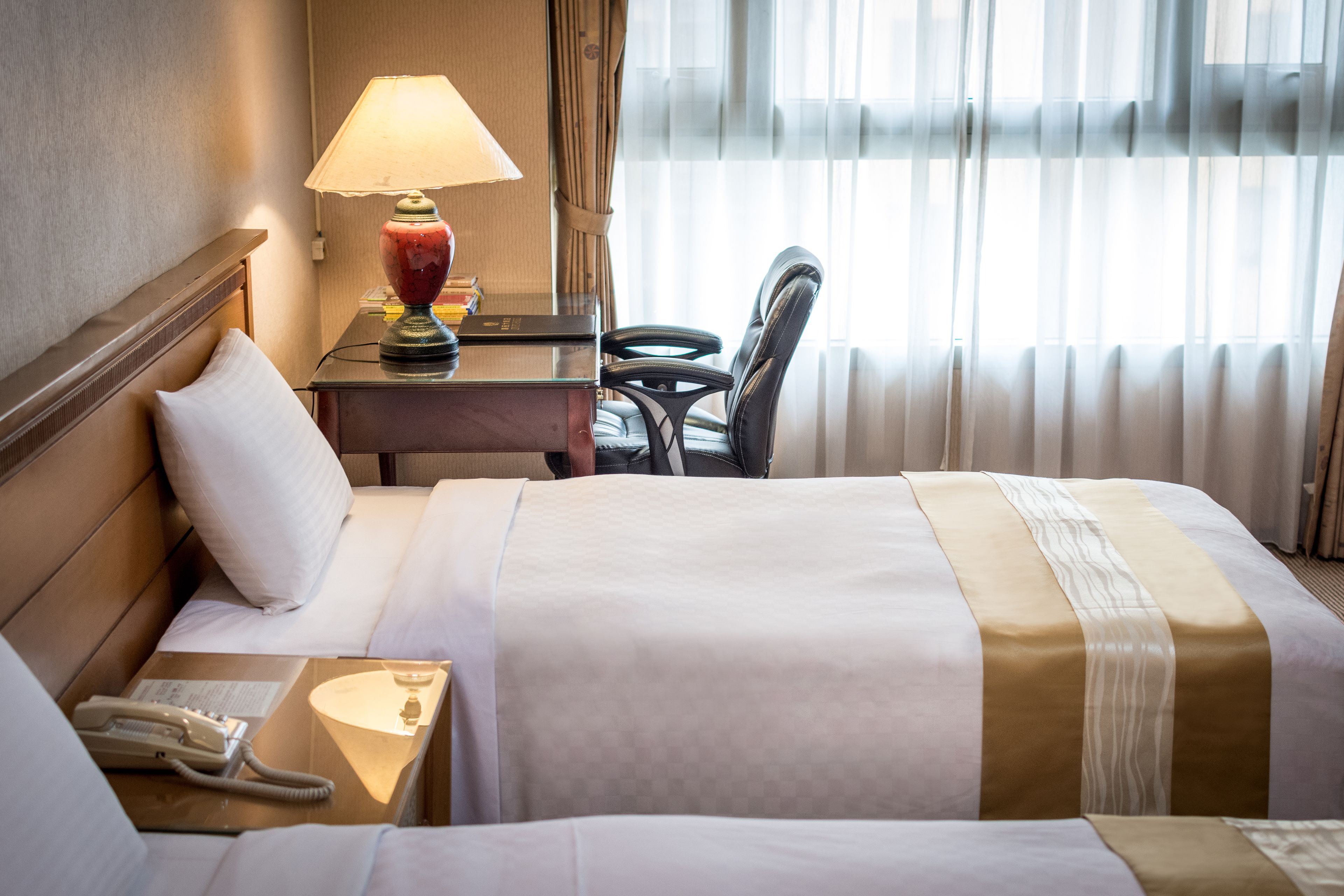 Ein Hotelzimmer mit Bett, Nachttisch mit Lampe, Schreibtisch und Stuhl.