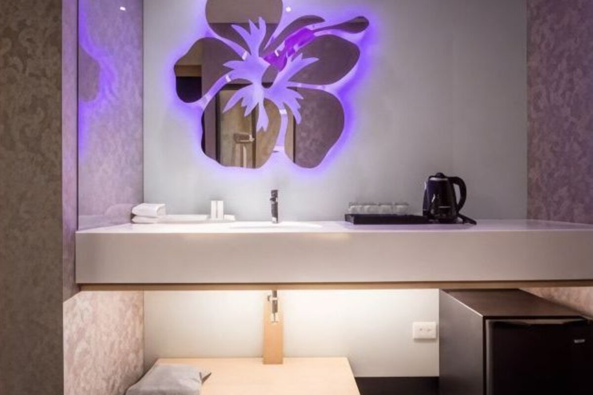 A modern bathroom with a large mirror, a sink, a coffee machine, and a towel on the counter.