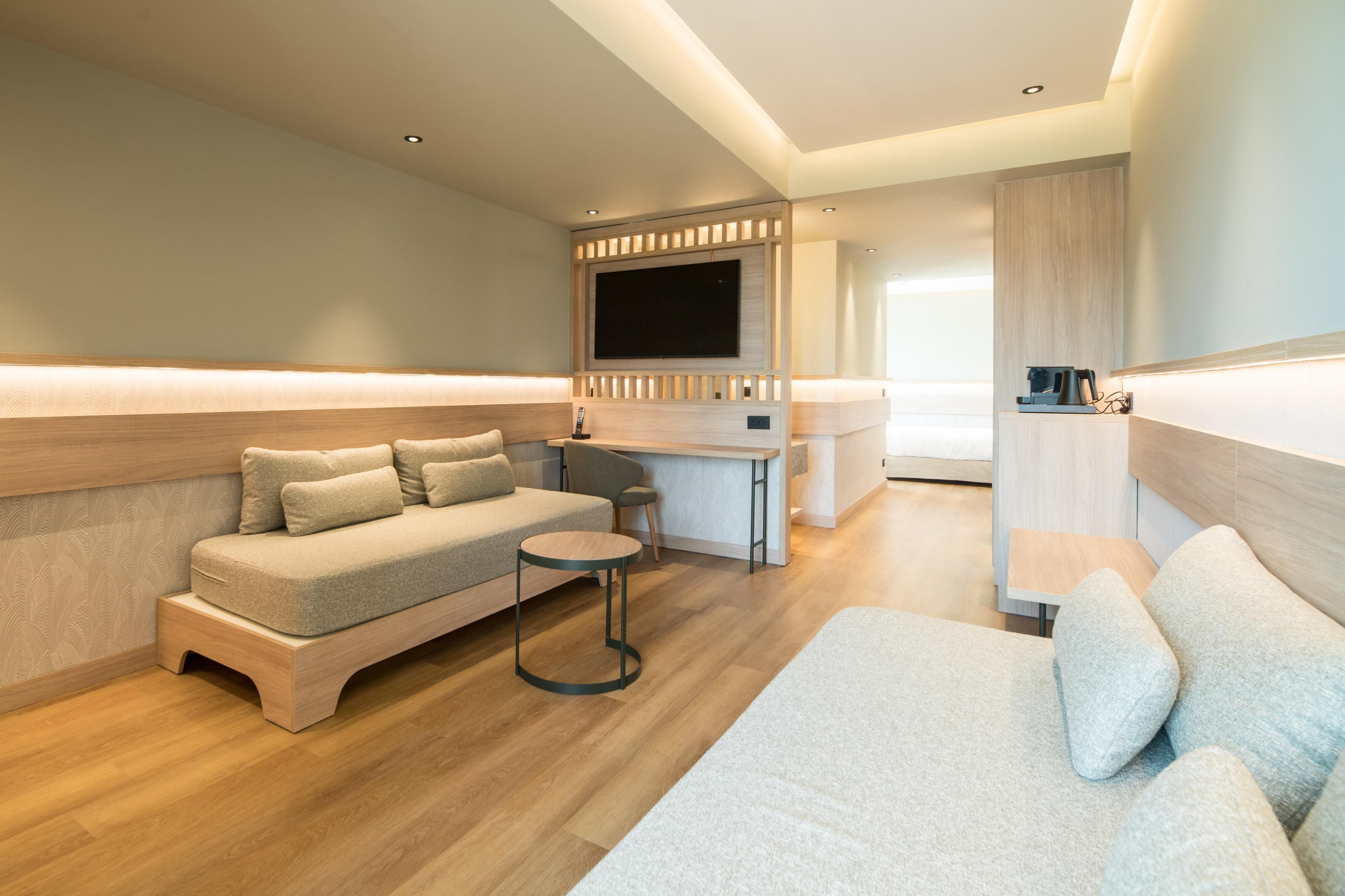 Un salon moderne avec un canapé d’angle, une petite table ronde et un téléviseur à écran plat fixé sur un panneau en bois.