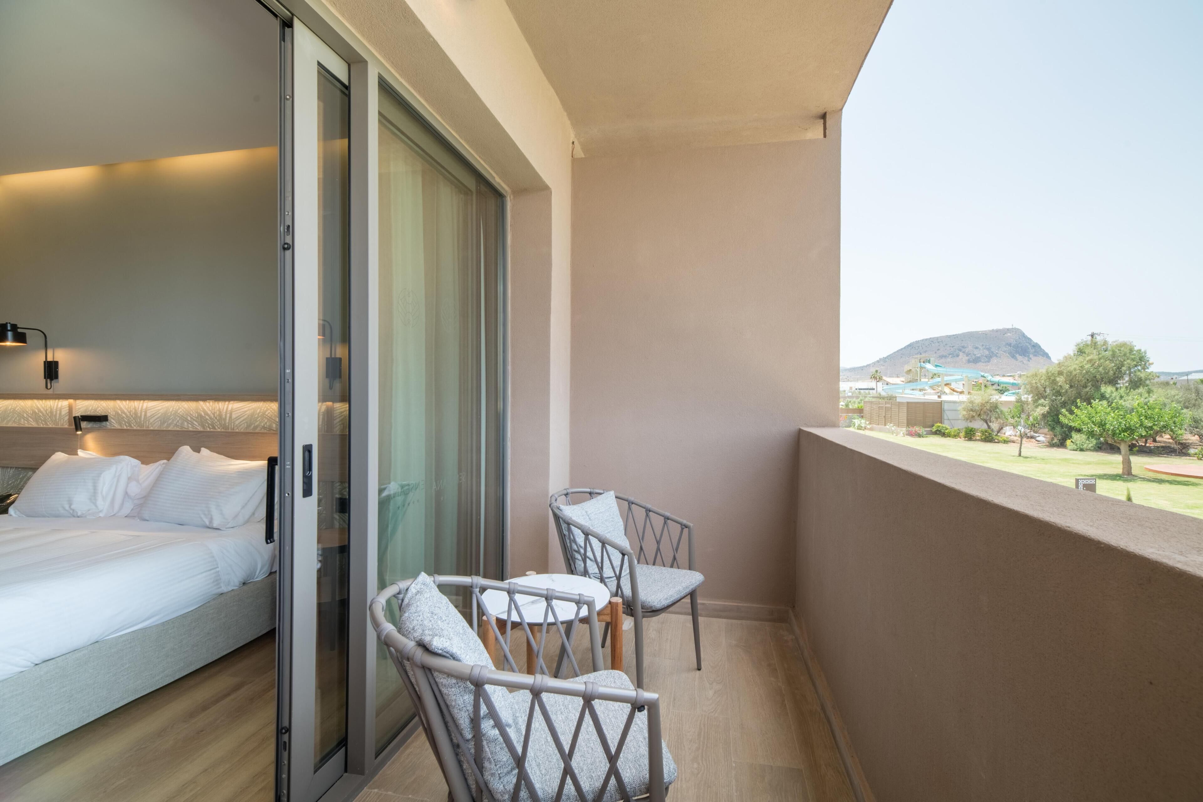 Un balcon avec un lit, deux chaises et une vue sur un paysage lointain.