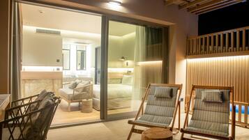 Una habitación de hotel moderna con un amplio ventanal corredero que da a un balcón, techo de madera y una cama con mesita de noche.