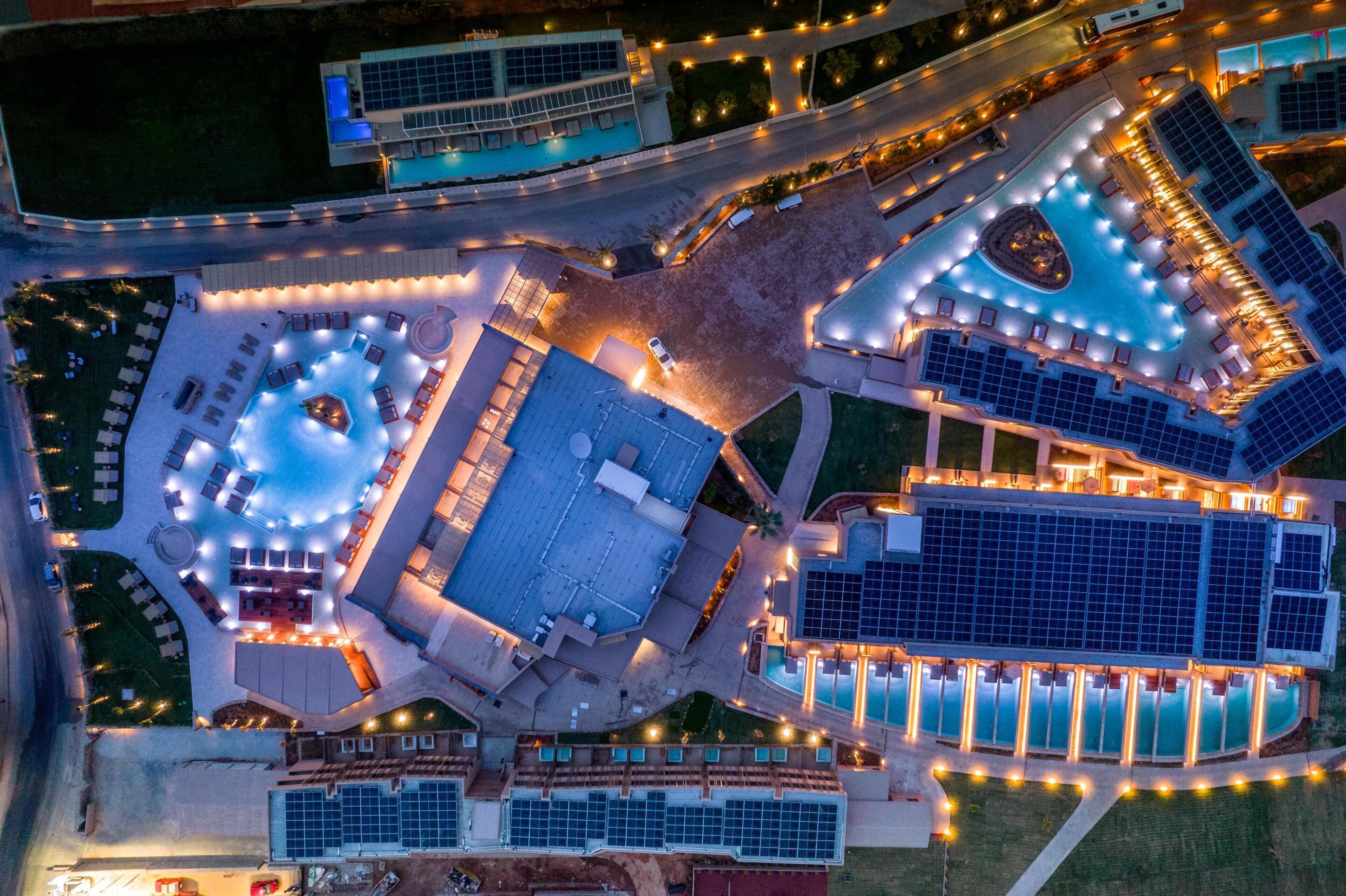 Luchtfoto van een hotel met meerdere zwembaden, zonnepanelen en buitenterrassen.