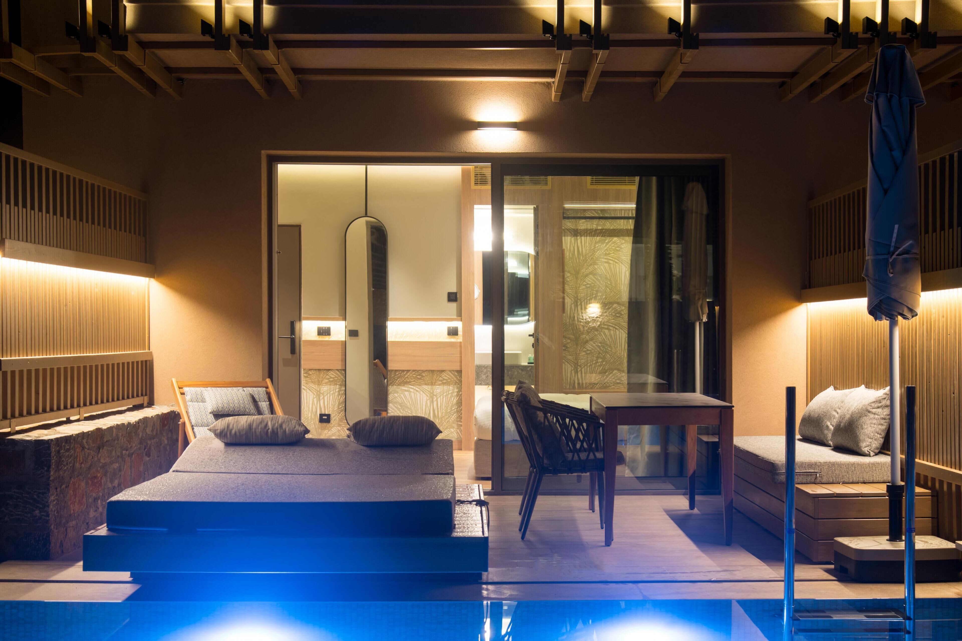 Une chambre moderne avec un lit, une petite table et une chaise. Une porte vitrée donne accès à une autre pièce.