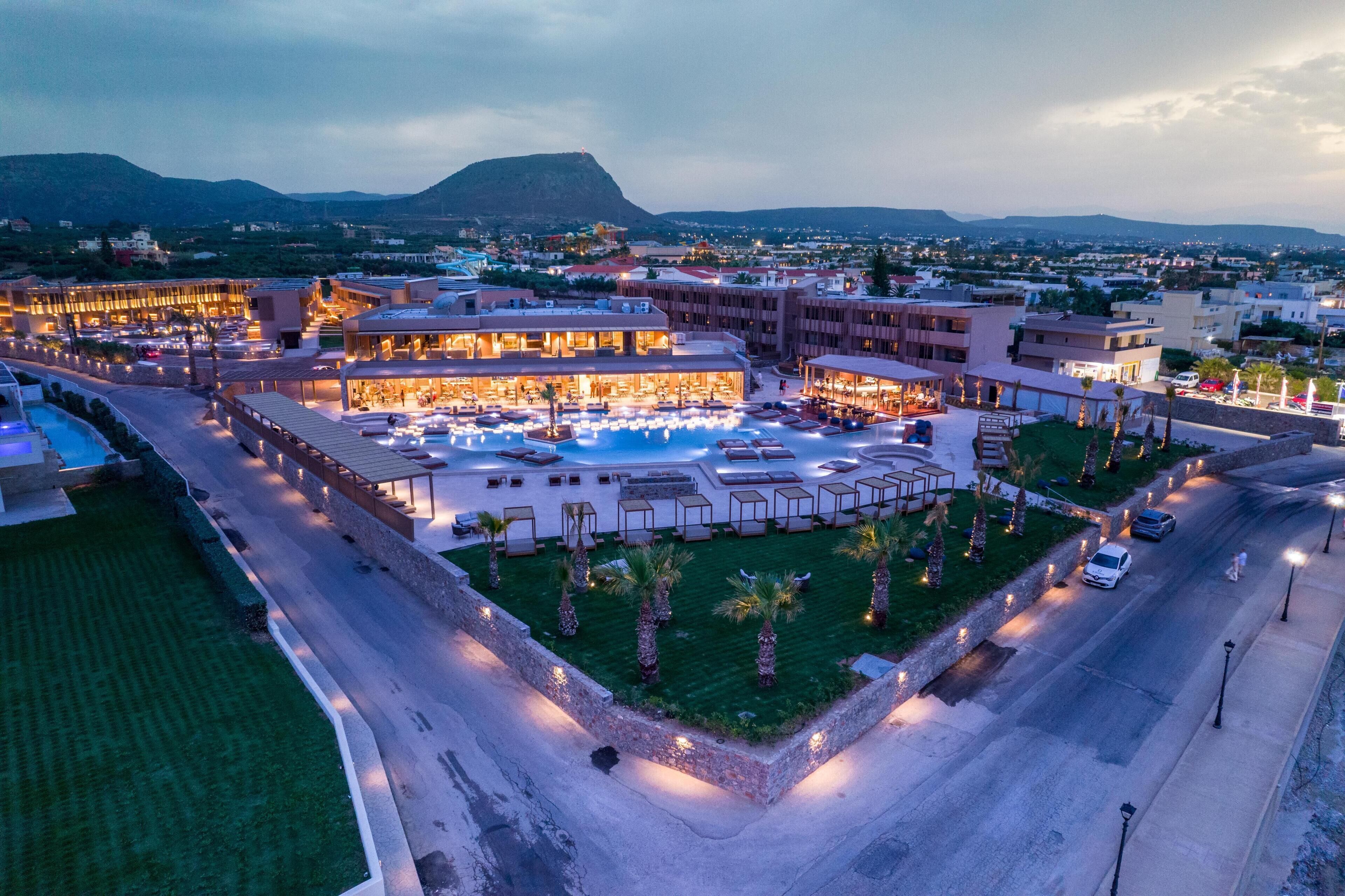 A resort with a large pool area, multiple buildings, and a view of distant mountains.