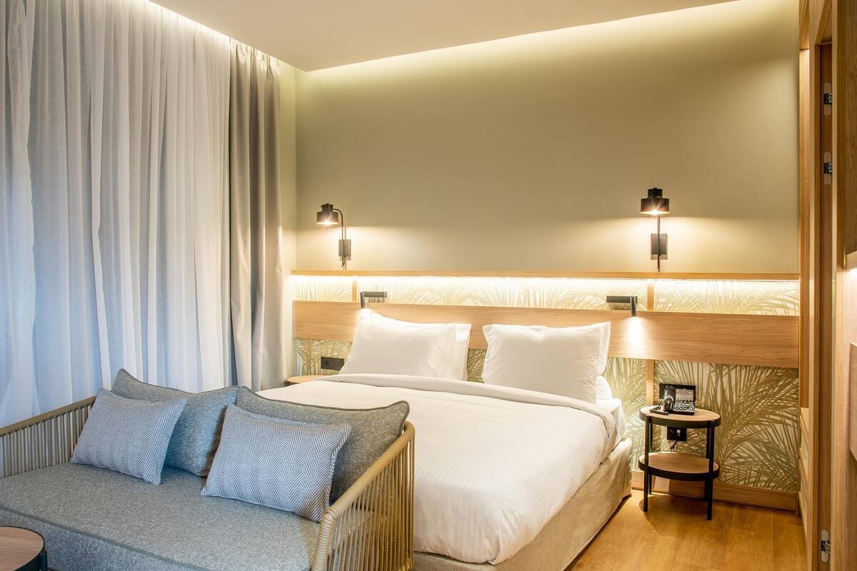 Une chambre d’hôtel avec un lit, un canapé, deux tables de chevet et une lampe.