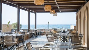 Área de refeições ao ar livre com móveis de vime e luminárias pendentes, com vista para o mar.