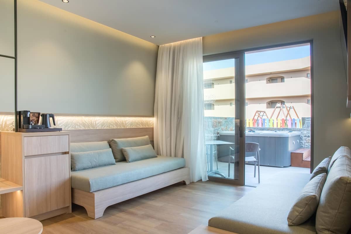 Une chambre d’hôtel moderne avec un canapé, un petit bureau et une vue sur un jacuzzi extérieur.