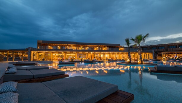 Um hotel com uma grande piscina ao ar livre, áreas de estar e fachada bem iluminada.
