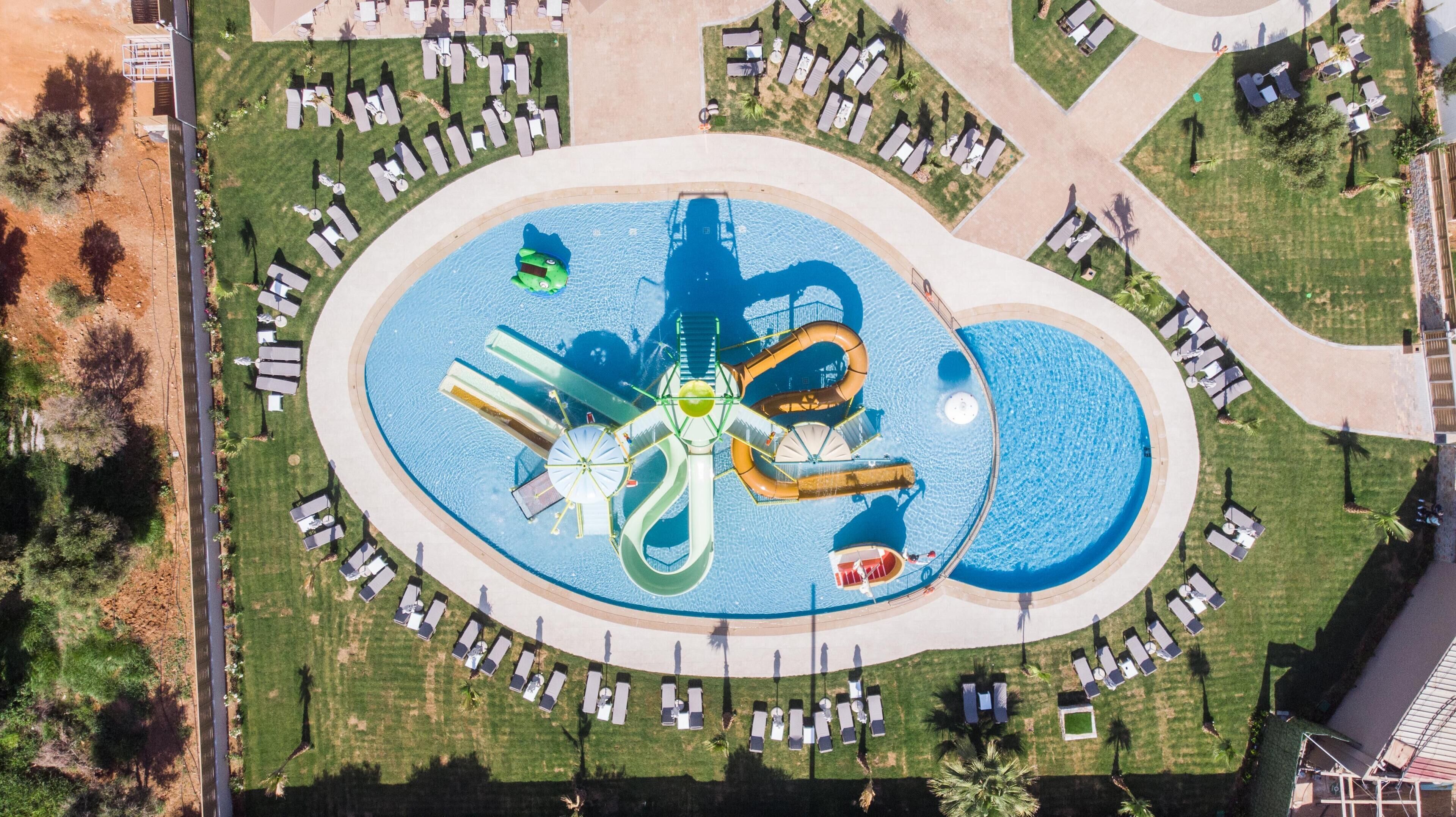 Luchtbeeld van een waterpark met meerdere glijbanen en zwembaden, omringd door terrasjes en wandelpaden.