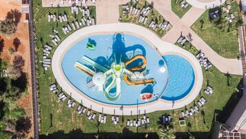 Luchtbeeld van een waterpark met meerdere glijbanen en zwembaden, omringd door terrasjes en wandelpaden.