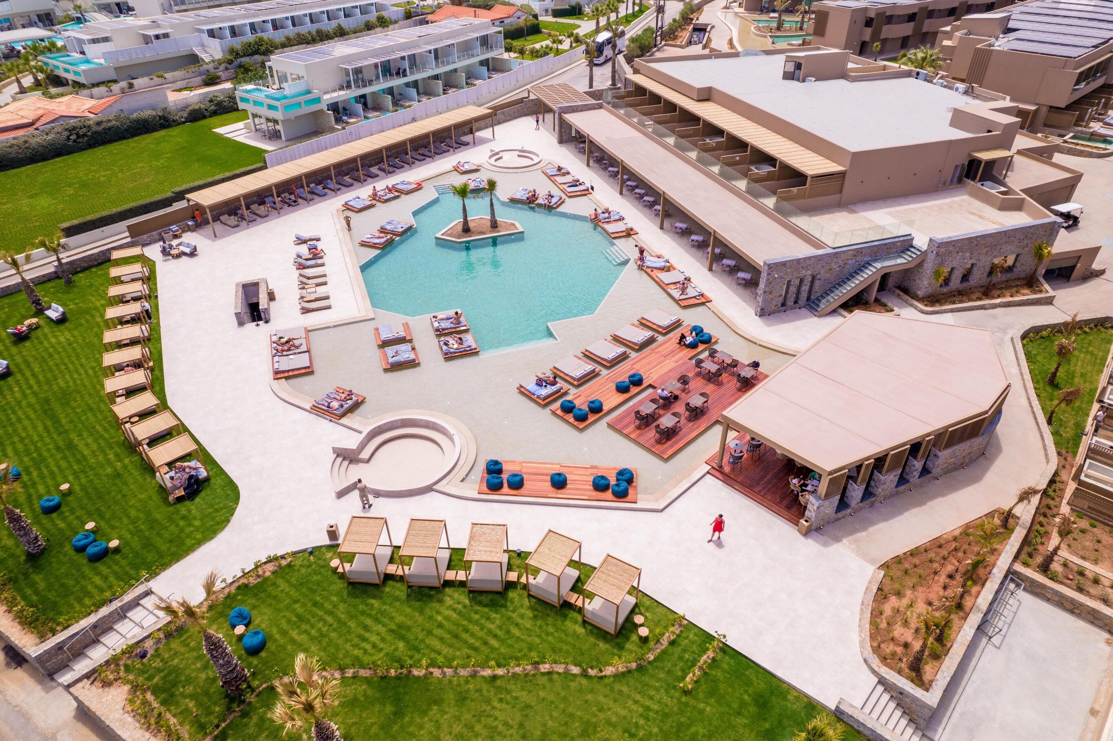 An aerial view of a hotel with a central pool, outdoor seating areas, and a landscaped garden.