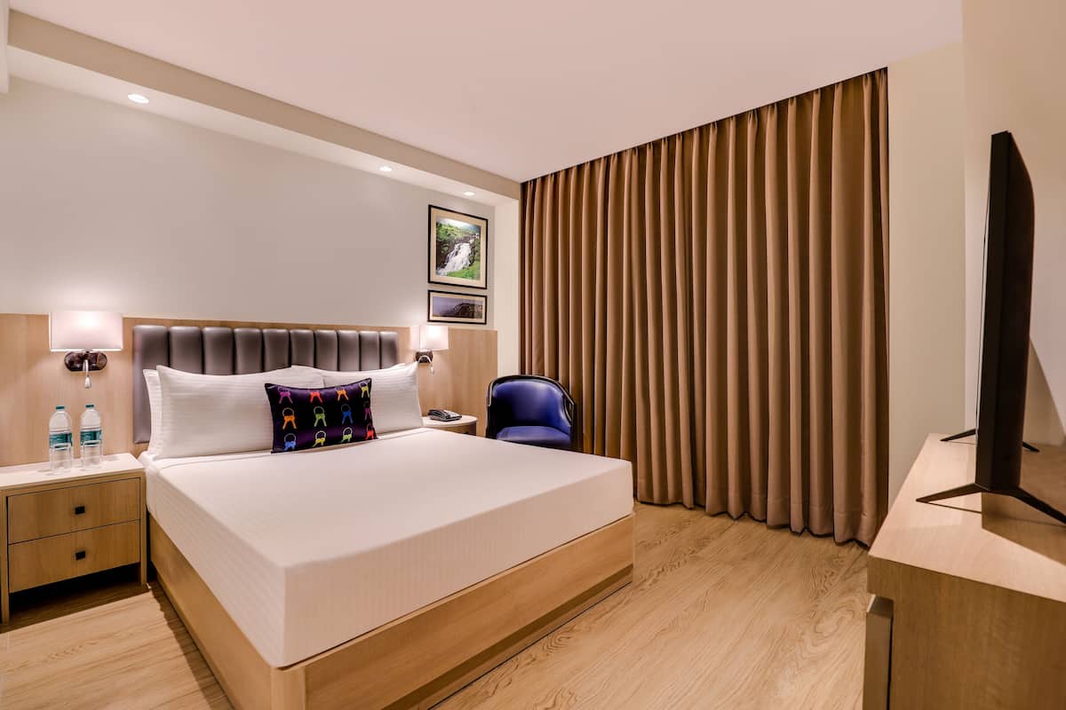 Habitación de hotel con una cama grande, mesitas de noche, un televisor de pantalla plana y un ventanal con cortinas.
