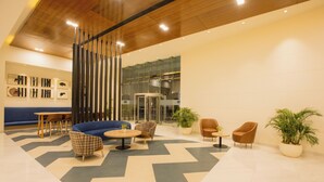 A modern lobby with a geometric patterned floor, a blue sofa, and several seating options including a checkered chair and a brown armchair. - Keys Prima by Lemon Tree Hotels, Pimpri Pune (Pune)