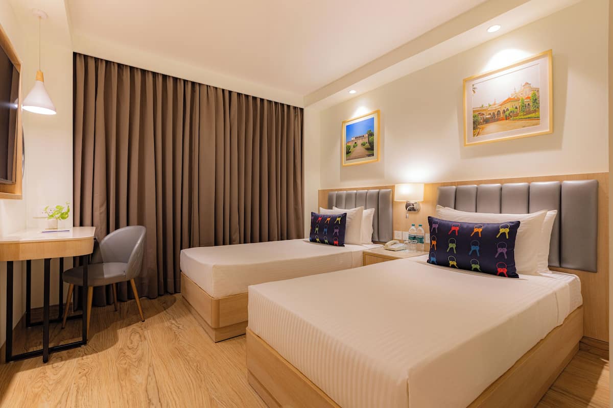 Habitación de hotel con dos camas, un escritorio, una silla y un ventanal grande con cortinas.
